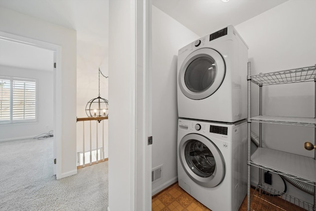 washroom with laundry area, stacked washer and dryer, baseboards, carpet, and a notable chandelier