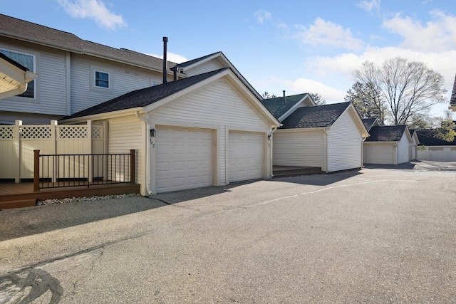 exterior space with fence, a deck, roof with shingles, an attached garage, and driveway