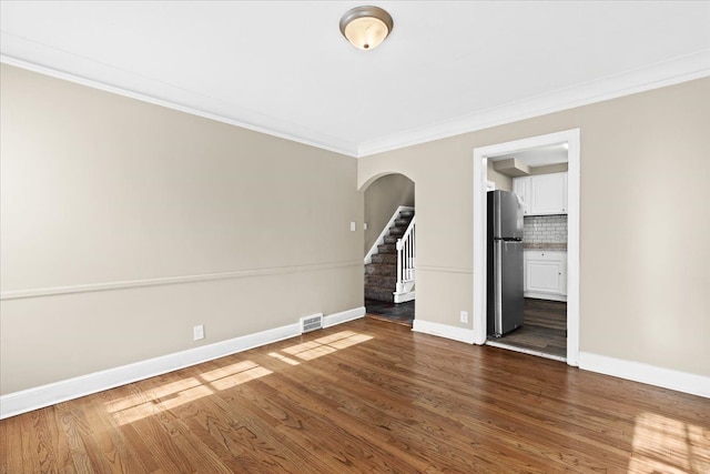 unfurnished bedroom featuring stainless steel refrigerator, ensuite bath, dark hardwood / wood-style flooring, and ornamental molding