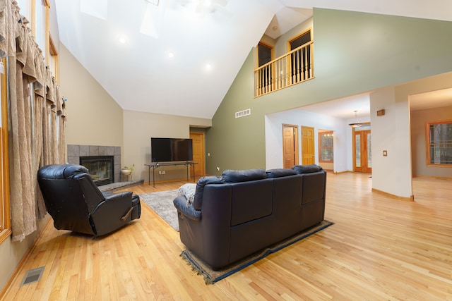 living room with a tile fireplace, high vaulted ceiling, a skylight, and light wood-type flooring