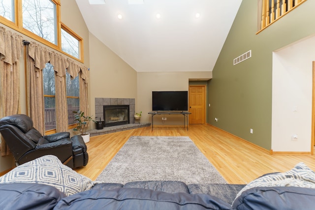 living room featuring a tiled fireplace, high vaulted ceiling, and hardwood / wood-style flooring