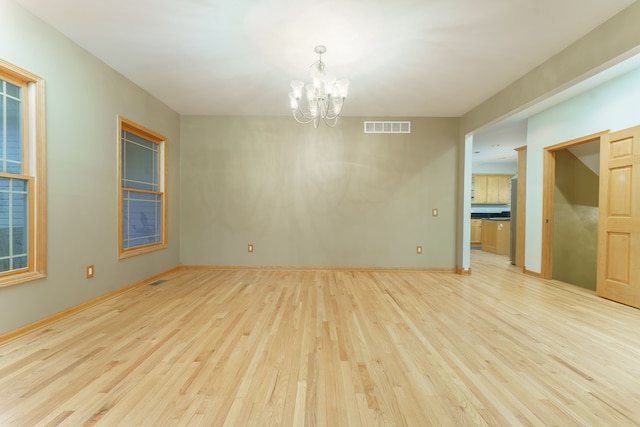 spare room featuring plenty of natural light, a notable chandelier, and light wood-type flooring