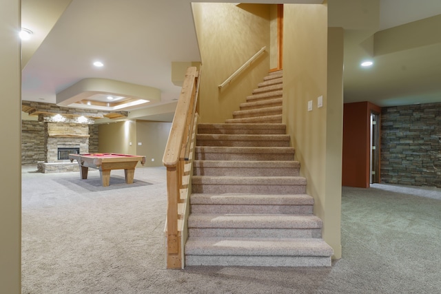 staircase with a tray ceiling, a stone fireplace, carpet floors, and billiards