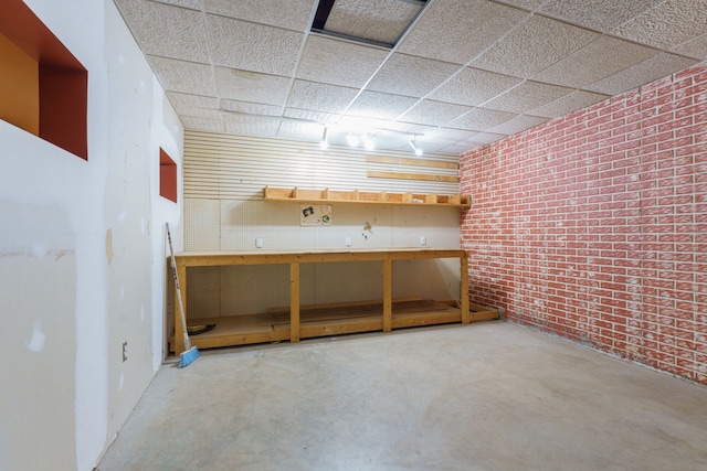 basement featuring a workshop area, a paneled ceiling, and brick wall