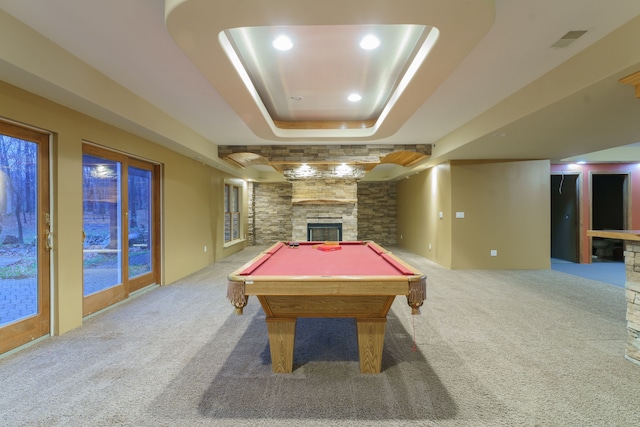 rec room with a raised ceiling, light colored carpet, a stone fireplace, and pool table