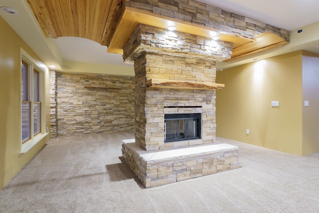 unfurnished living room featuring a raised ceiling, a stone fireplace, wooden ceiling, and carpet