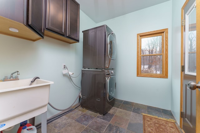 clothes washing area with cabinets, stacked washing maching and dryer, and sink