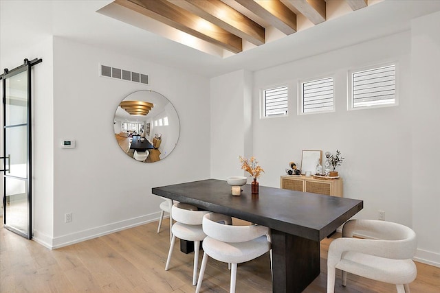 dining room featuring beamed ceiling, a barn door, and light hardwood / wood-style floors