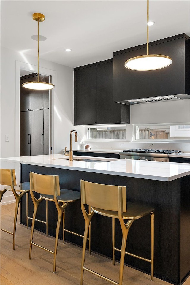 kitchen featuring stainless steel range, extractor fan, sink, pendant lighting, and light hardwood / wood-style floors