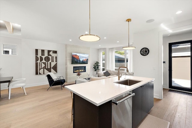 kitchen with pendant lighting, light wood-type flooring, sink, and a kitchen island with sink