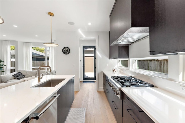 kitchen featuring wall chimney exhaust hood, stainless steel appliances, sink, pendant lighting, and light hardwood / wood-style flooring