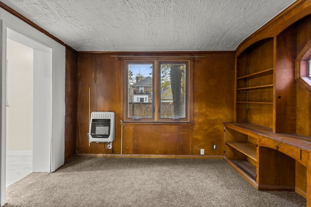 empty room featuring heating unit, wood walls, carpet, and a textured ceiling