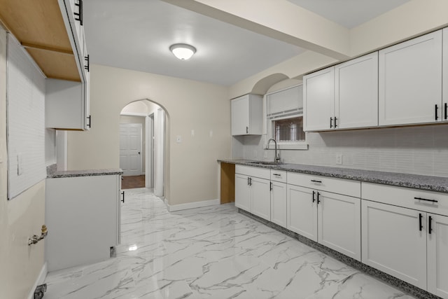 kitchen with decorative backsplash, white cabinetry, sink, and stone counters