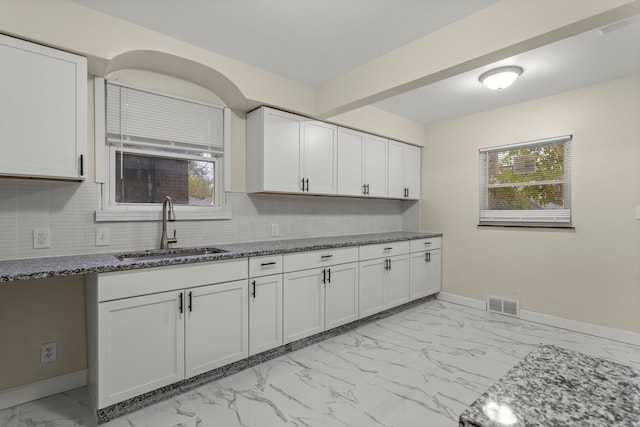 kitchen with white cabinets, backsplash, dark stone countertops, and sink