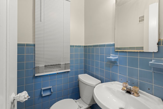 bathroom with toilet, sink, and tile walls