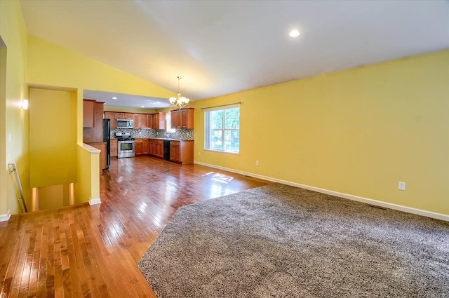 unfurnished living room with hardwood / wood-style flooring, a notable chandelier, and lofted ceiling