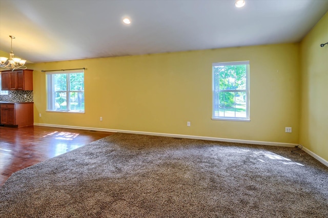 empty room with a notable chandelier, dark hardwood / wood-style floors, a wealth of natural light, and vaulted ceiling