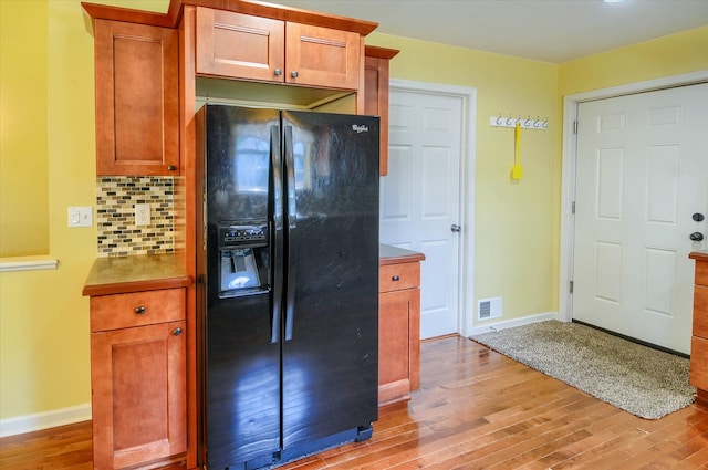 kitchen with backsplash, light hardwood / wood-style floors, and black fridge