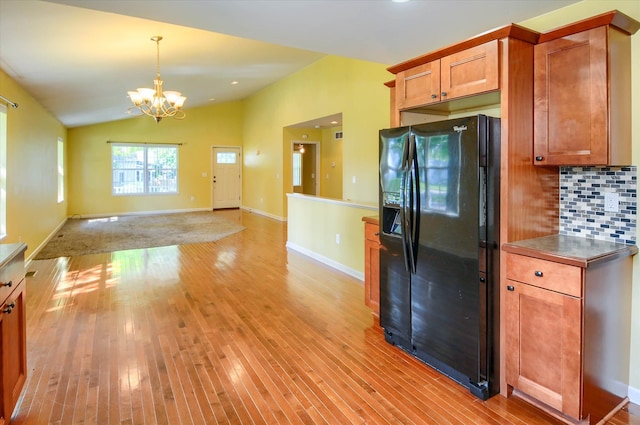 kitchen with a notable chandelier, backsplash, lofted ceiling, black fridge with ice dispenser, and light wood-type flooring