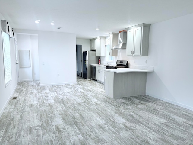 kitchen featuring wall chimney range hood, sink, light hardwood / wood-style flooring, appliances with stainless steel finishes, and kitchen peninsula