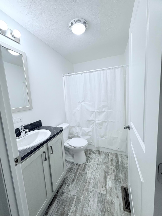 bathroom featuring a textured ceiling, vanity, hardwood / wood-style flooring, and toilet