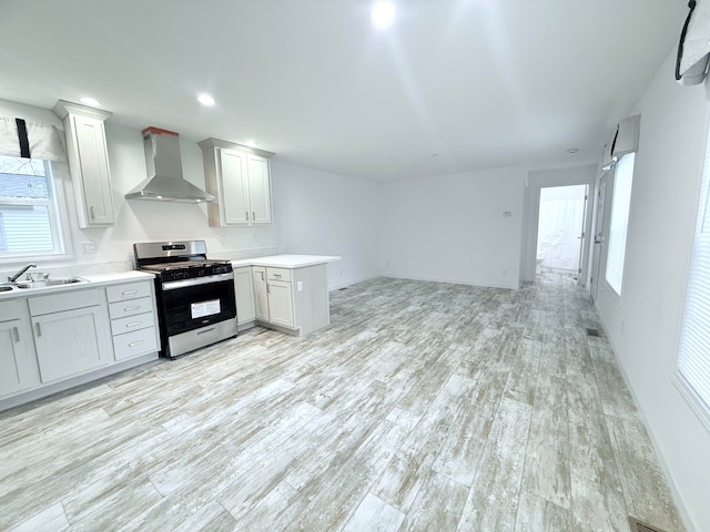 kitchen with stainless steel range with gas cooktop, sink, wall chimney exhaust hood, and light hardwood / wood-style floors