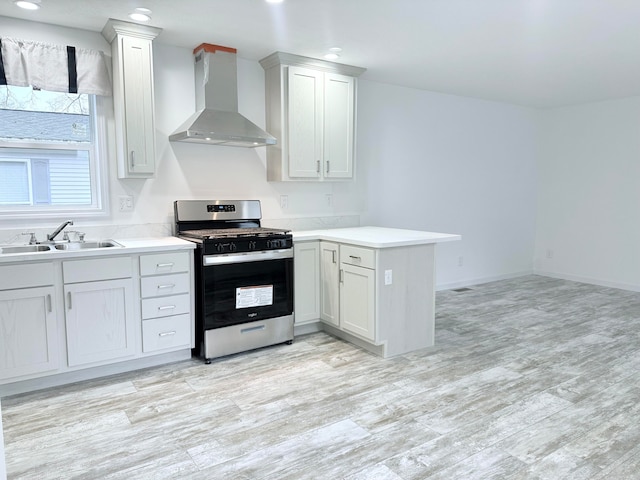 kitchen with gas range, sink, wall chimney range hood, kitchen peninsula, and light hardwood / wood-style floors