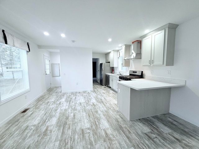 kitchen with sink, stainless steel appliances, wall chimney range hood, kitchen peninsula, and light hardwood / wood-style floors