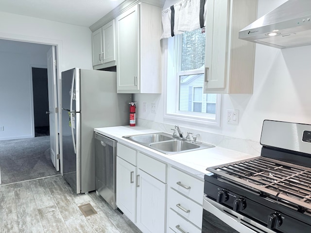 kitchen with white cabinetry, sink, wall chimney range hood, light hardwood / wood-style flooring, and appliances with stainless steel finishes