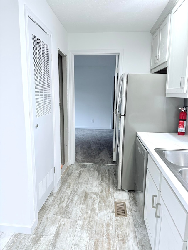 kitchen with light wood-type flooring, white cabinetry, and stainless steel dishwasher