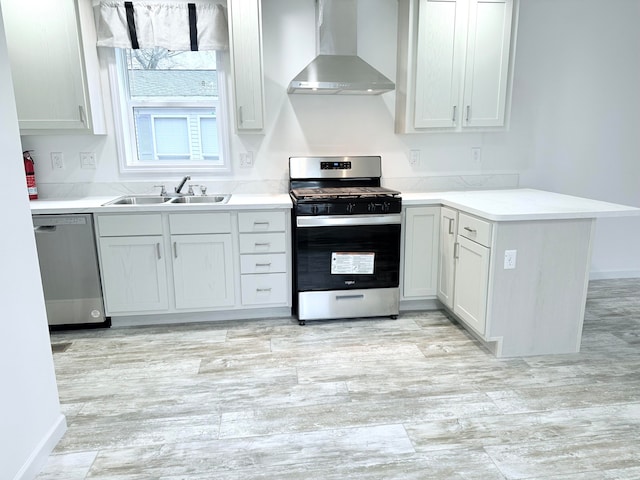 kitchen featuring kitchen peninsula, appliances with stainless steel finishes, sink, wall chimney range hood, and white cabinets