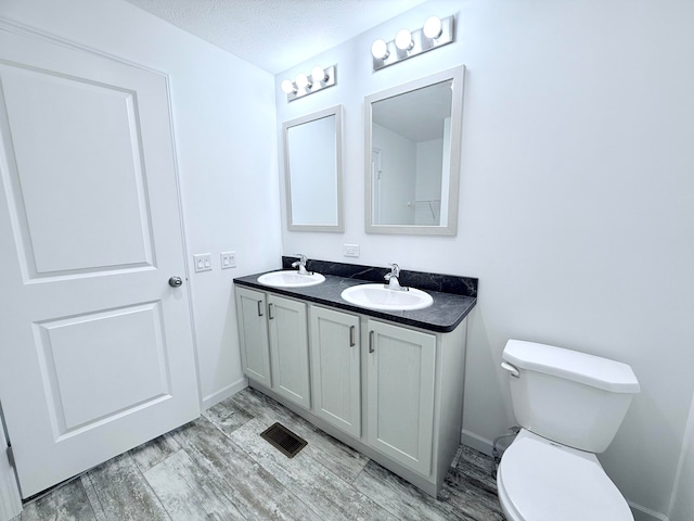 bathroom with vanity, toilet, wood-type flooring, and a textured ceiling