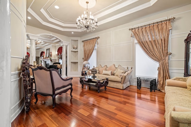 living area featuring wood finished floors, arched walkways, a decorative wall, a raised ceiling, and ornate columns