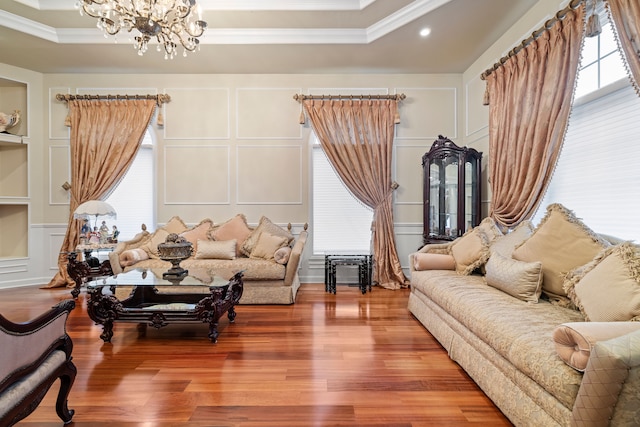 living area with an inviting chandelier, a decorative wall, wood finished floors, and ornamental molding