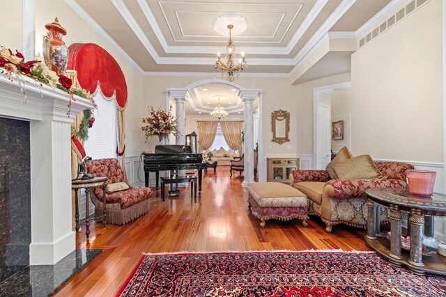 living area with a chandelier, a wainscoted wall, decorative columns, arched walkways, and a raised ceiling