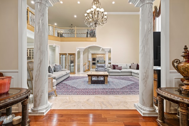 living room featuring a chandelier, ornamental molding, decorative columns, a towering ceiling, and arched walkways