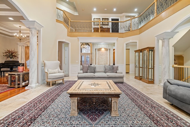 living area featuring crown molding, a wainscoted wall, arched walkways, a decorative wall, and ornate columns