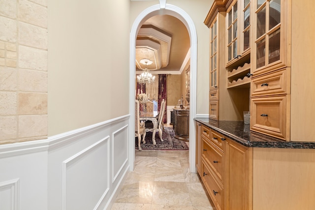 interior space featuring a wainscoted wall, arched walkways, crown molding, a decorative wall, and a chandelier