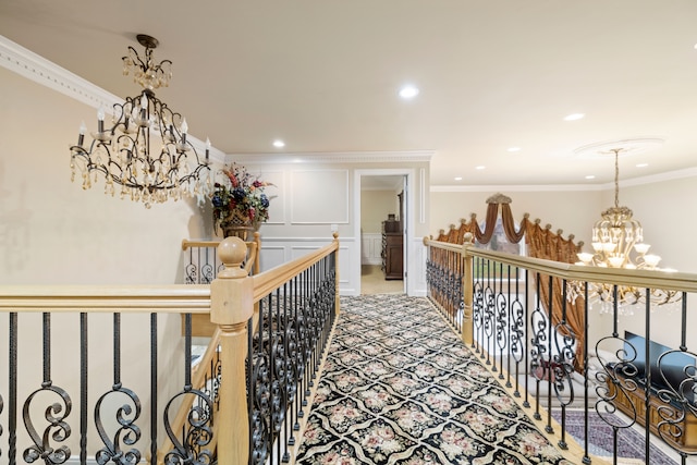 hall featuring an inviting chandelier, crown molding, a decorative wall, an upstairs landing, and light colored carpet