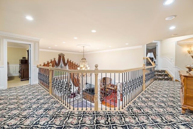 hall featuring carpet, a wainscoted wall, crown molding, a decorative wall, and a notable chandelier