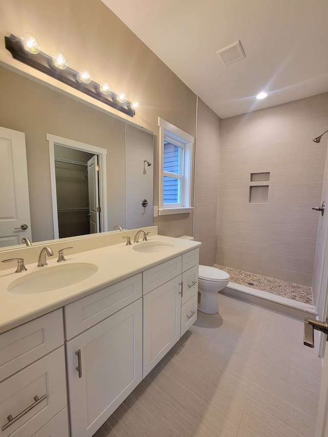 bathroom with a tile shower, vanity, and toilet