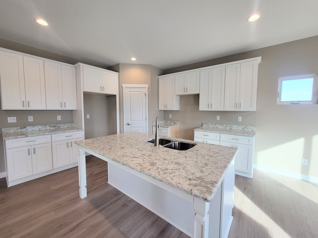 kitchen featuring white cabinetry, sink, light stone counters, light hardwood / wood-style floors, and a kitchen island with sink