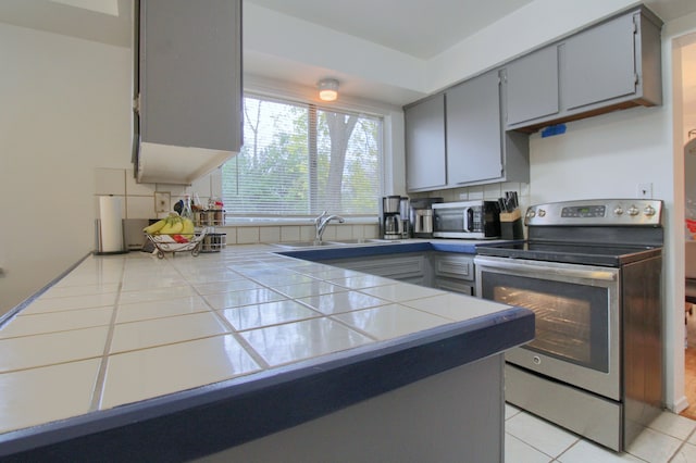 kitchen with tile counters, light tile patterned floors, sink, and appliances with stainless steel finishes