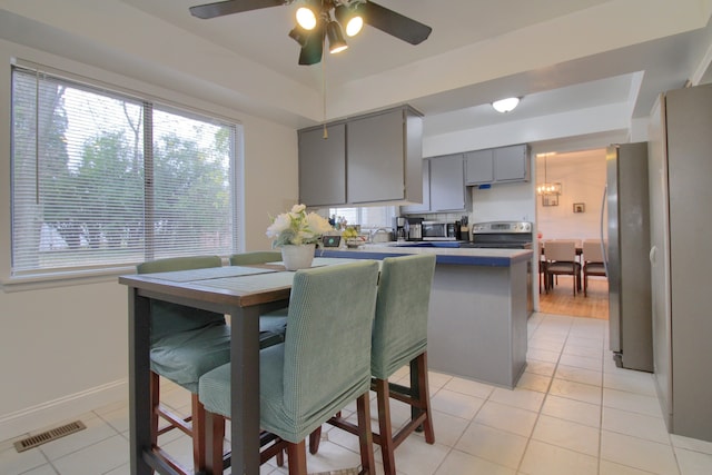 kitchen with kitchen peninsula, light tile patterned floors, stainless steel appliances, and gray cabinets