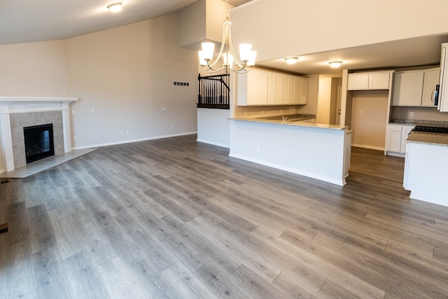 kitchen with a tile fireplace, hardwood / wood-style floors, white cabinets, hanging light fixtures, and a notable chandelier