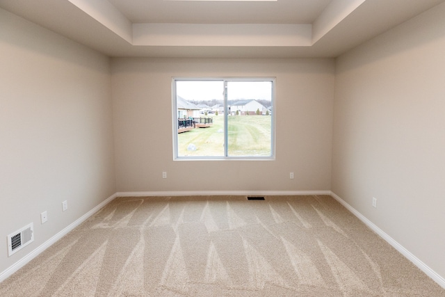 carpeted empty room with a tray ceiling, visible vents, and baseboards