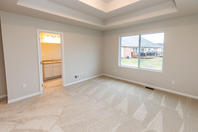 unfurnished bedroom with light carpet, a tray ceiling, visible vents, and baseboards