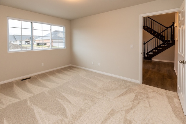 carpeted spare room featuring visible vents, baseboards, and stairs