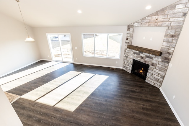 unfurnished living room with plenty of natural light, dark hardwood / wood-style flooring, vaulted ceiling, and a stone fireplace