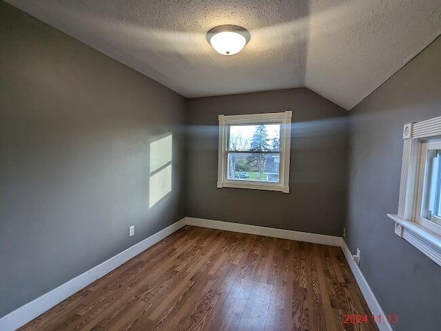 unfurnished room featuring wood-type flooring, a textured ceiling, and vaulted ceiling